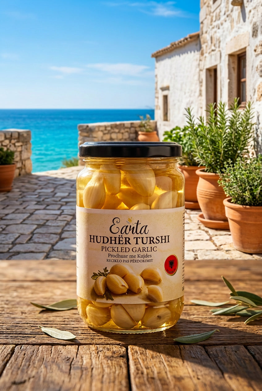 A jar of Earta Pickled Garlic with a black lid and white label, sitting on a cardboard box in a warehouse-like setting with other packaged goods in the background.